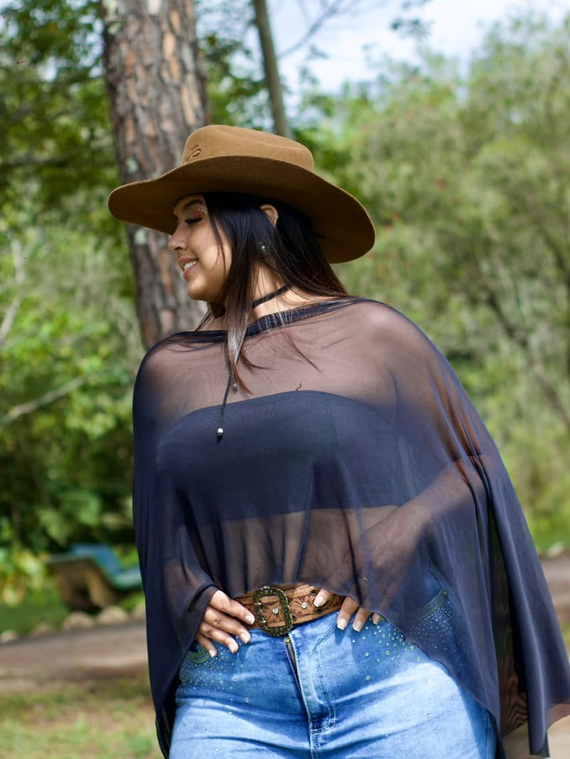 Mulher de chapéu e bata transparente sorrindo em ensaio ao ar livre