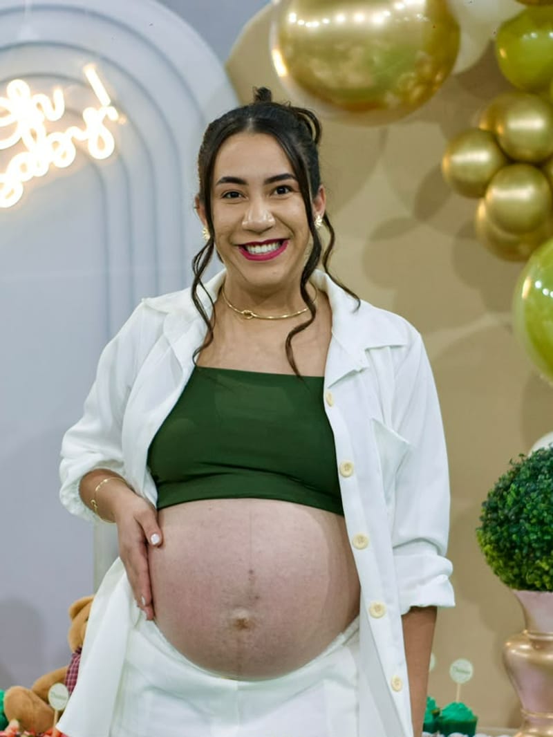 Gestante sorrindo com a mão na barriga em frente aos balões do chá de bebê