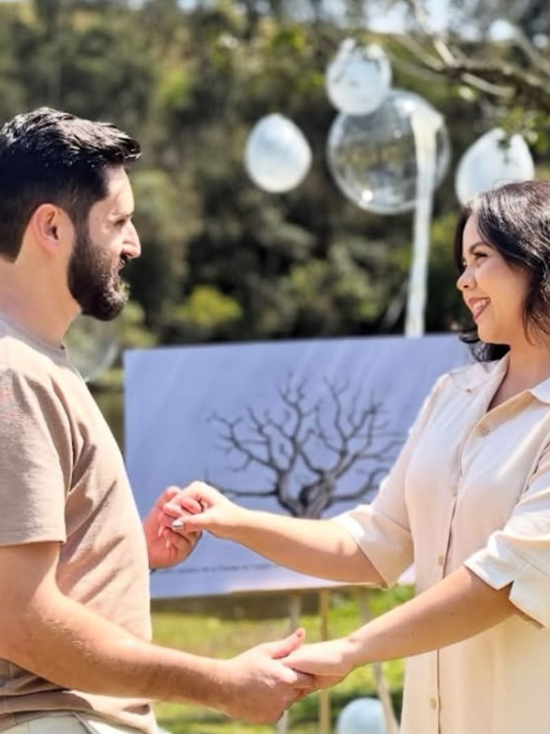 Casal de mãos dadas sorrindo no chá revelação, com balões brancos ao fundo